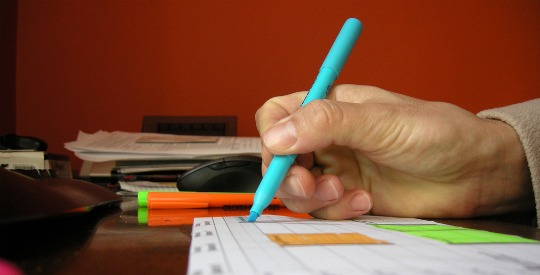 A picture of a hand holding a teal highlighter over a piece of paper.