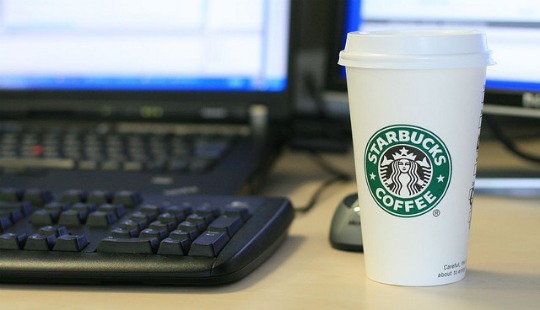 A Starbucks cup next to a computer screen and keyboard